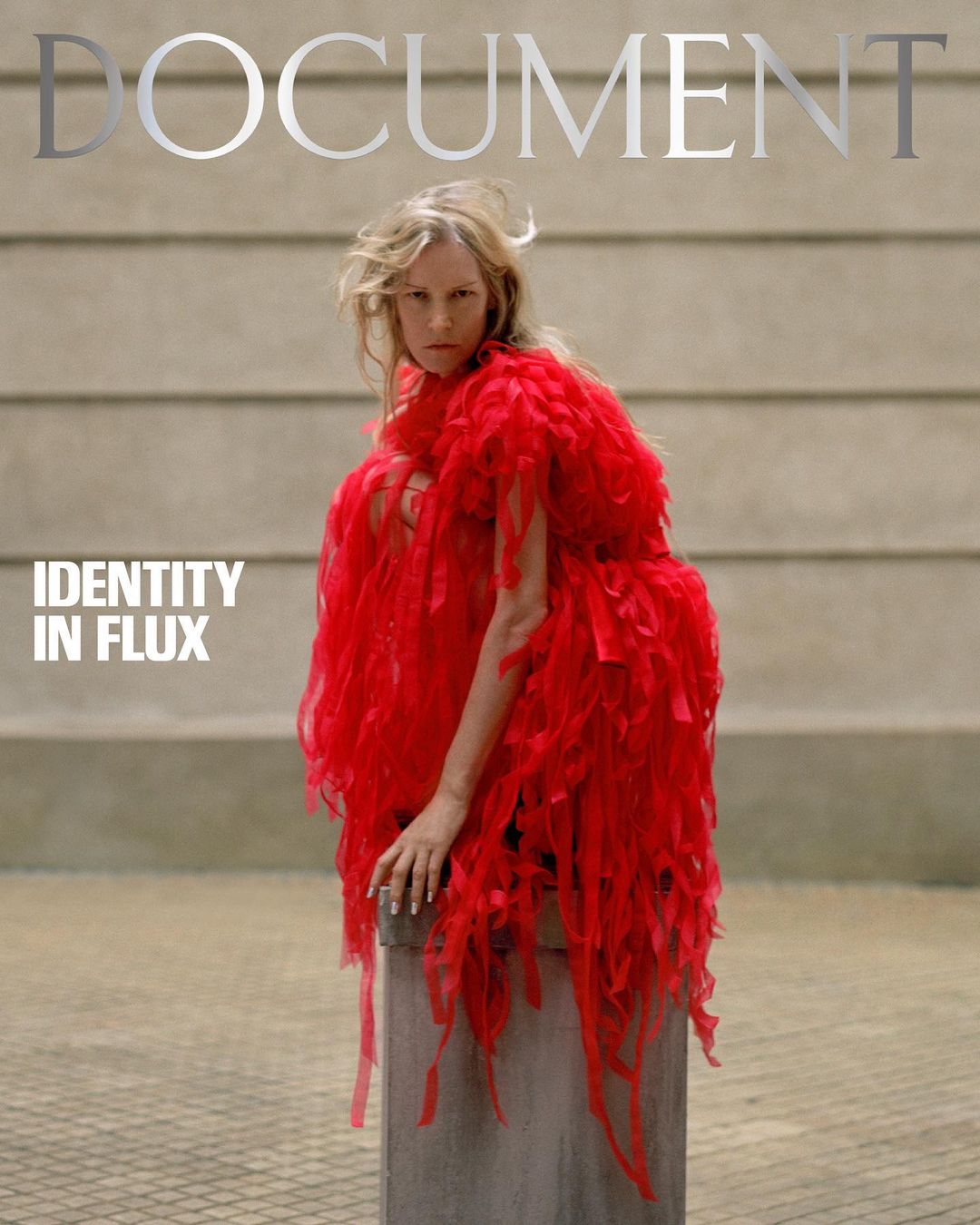 Blonde woman wearing a red, feathery dress poses on a concrete cylinder against a gray wall for a magazine cover titled 'Document'.