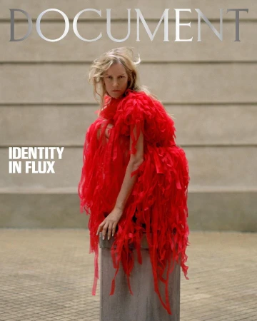 Blonde woman wearing a red, feathery dress poses on a concrete cylinder against a gray wall for a magazine cover titled 'Document'.
