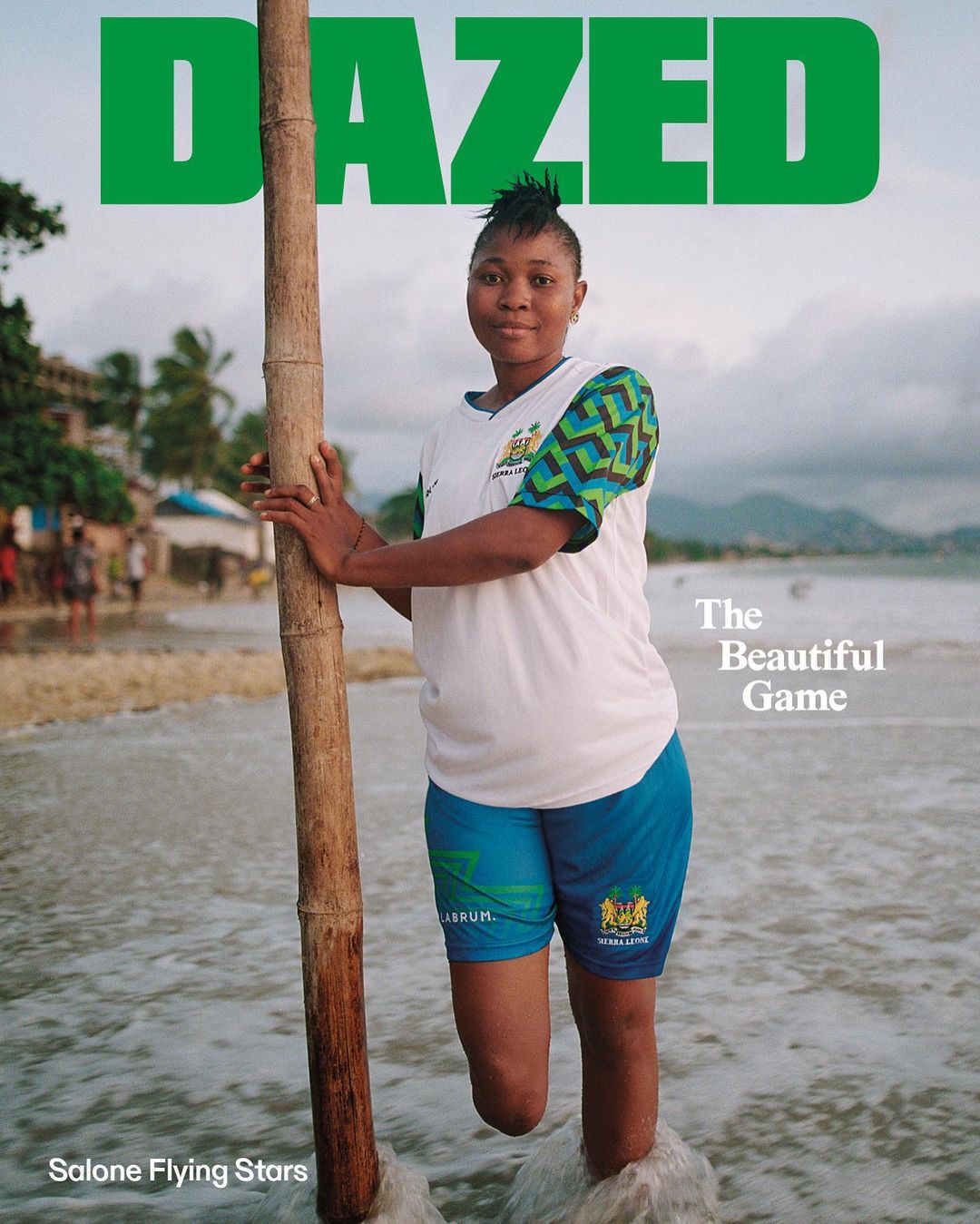 Magazine cover featuring a smiling woman standing in the ocean with a wooden pole, set against a blurred coastal backdrop.
