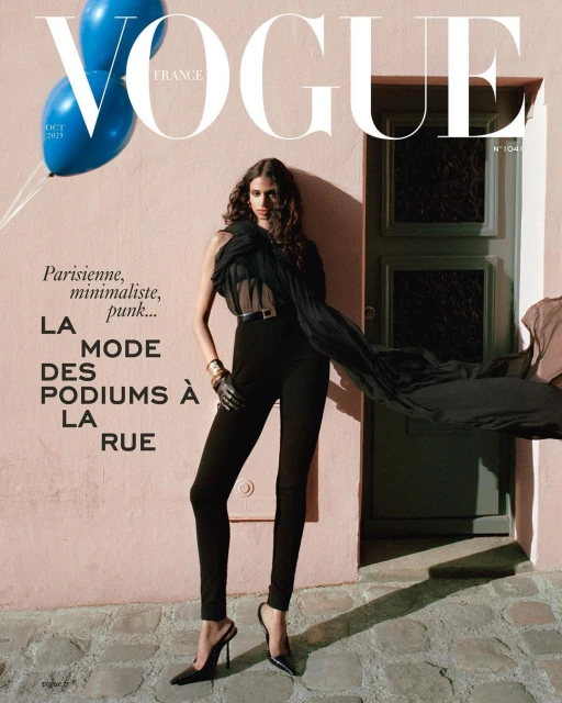 Vogue France cover features a woman in black attire standing on a cobblestone street, with blue balloons and magazine text.