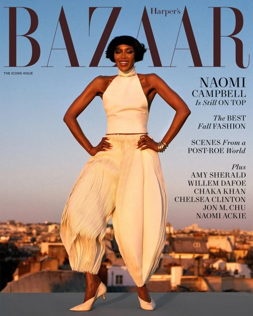 Naomi Campbell on the cover of Harper's Bazaar magazine, wearing a white halter top and billowing white pants, posing outdoors at sunset.
