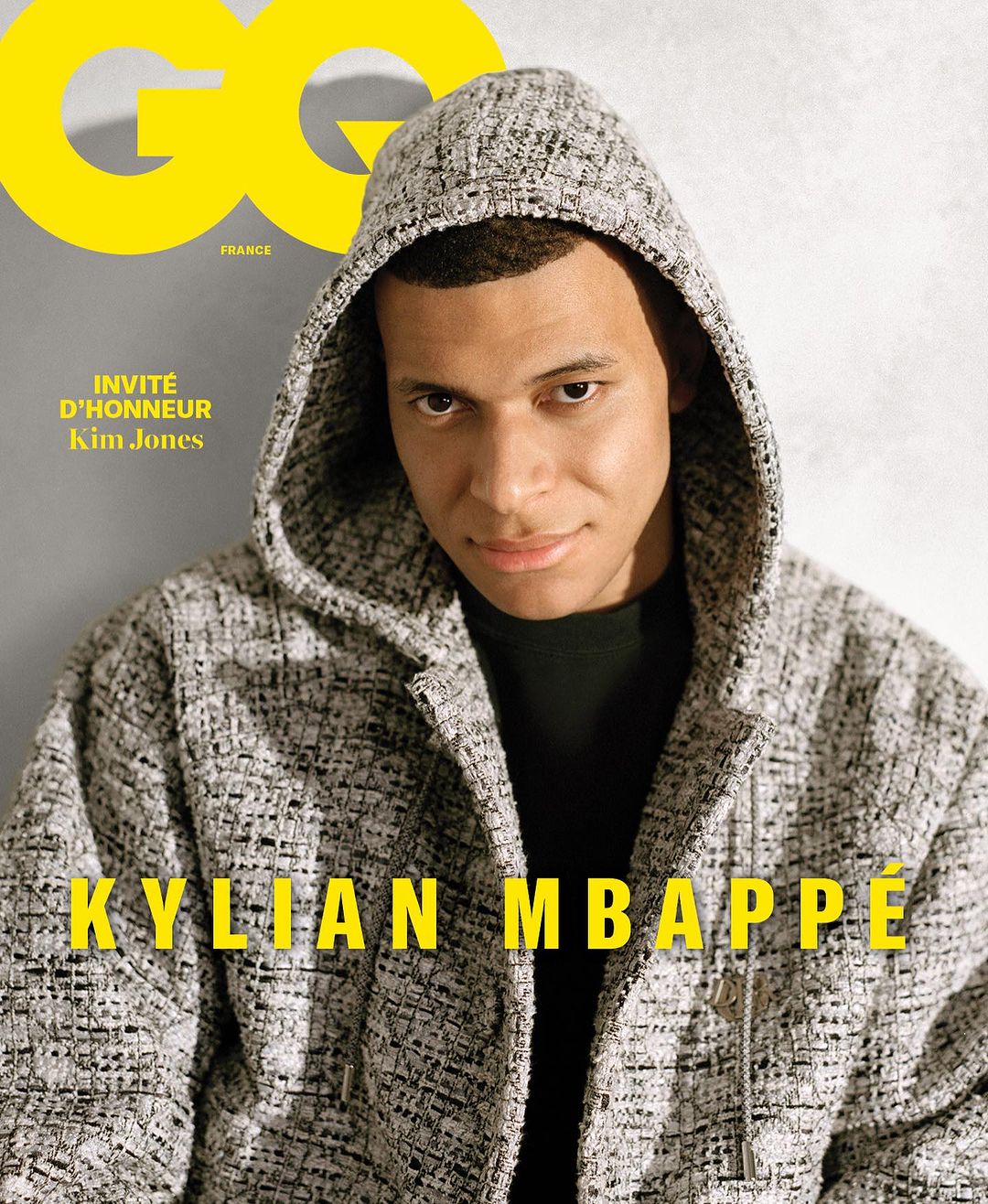 Kylian Mbappé on the cover of GQ France, posing in a hooded jacket with yellow text overlay on a grey background for a magazine cover.