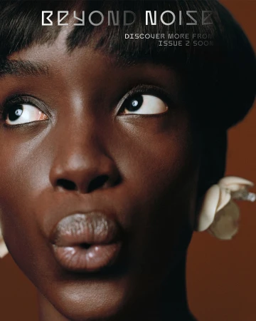 Close-up portrait of a dark-skinned adult female model with short black hair, wearing floral earrings, and looking upwards on a brown background.