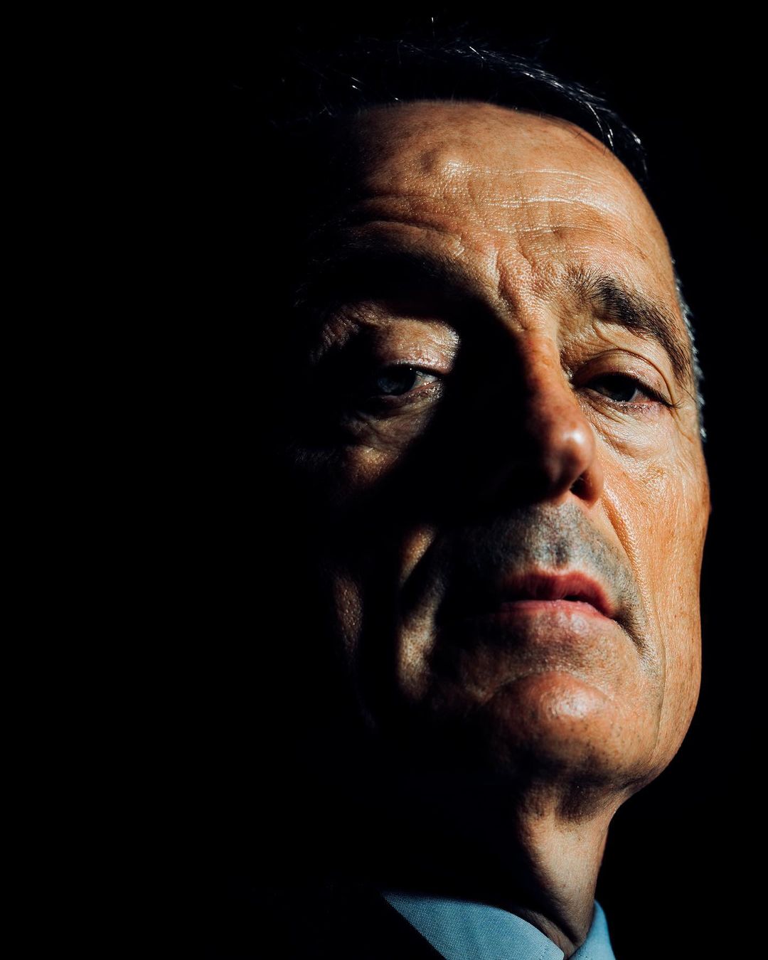 Close-up portrait of an older man with dramatic low-key lighting against a dark background, photographed by Malike Sidibe