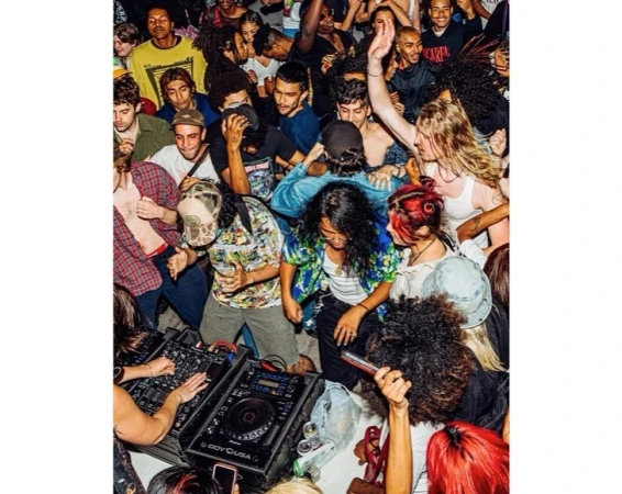 Energetic group of young adults dancing and enjoying a lively party, bathed in vibrant lighting with DJ equipment visible.