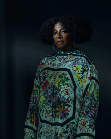 Portrait of an older Black woman wearing a patterned floral silk top against a dark moody background, photographed by Malike Sidibe.