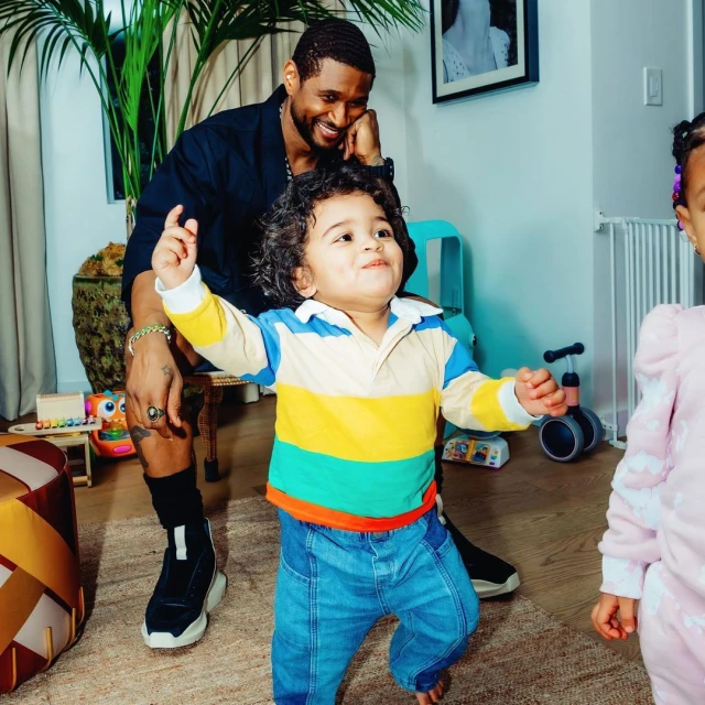 A parent and two children in a brightly lit home, with the primary focus on a toddler wearing a colorful striped shirt.