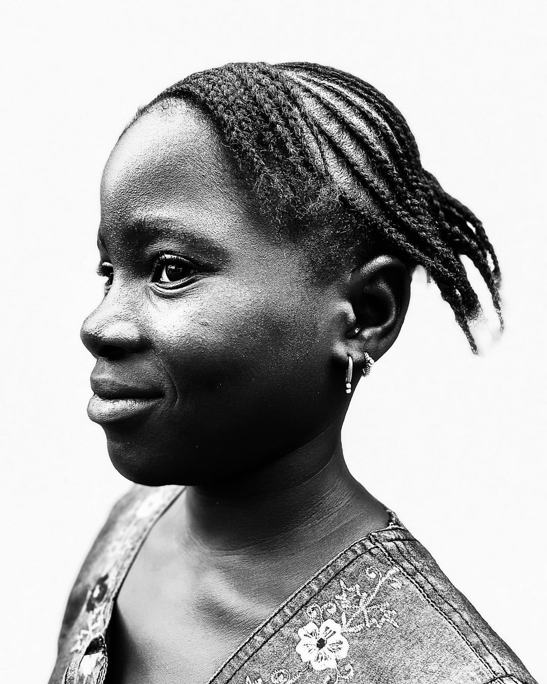 Portrait of a young African-descent woman with braided hair and a denim top, smiling slightly against a bright, neutral background.