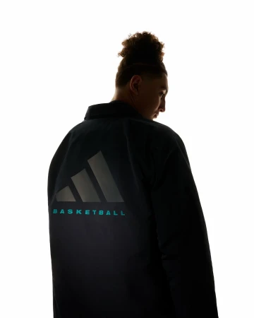 Silhouette portrait of a person with curly hair wearing a dark jacket with reflective Adidas Basketball logo on the back.