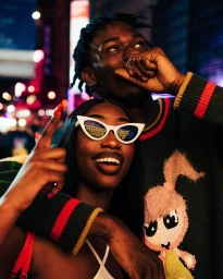 Portrait of a smiling Black woman in white cat-eye sunglasses and a man looking up in New York by Malike Sidibe.