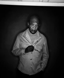 Portrait of Samuel L. Jackson in a button-down collared shirt holding eyeglasses against a dark background