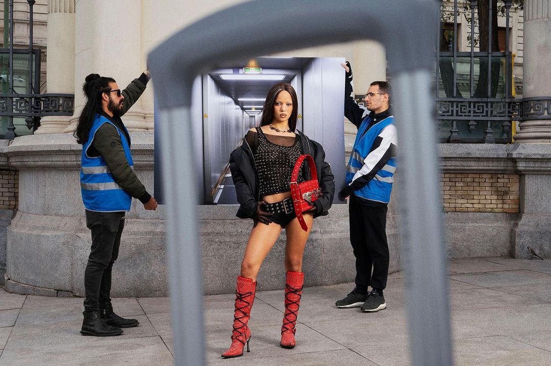 Fashionable woman poses outdoors framed by urban scene image held up by two uniformed men in front of building with a passerby.