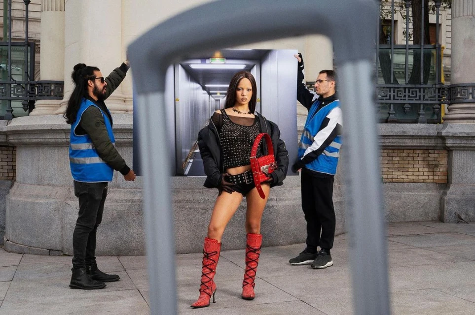 Fashionable woman poses outdoors framed by urban scene image held up by two uniformed men in front of building with a passerby.