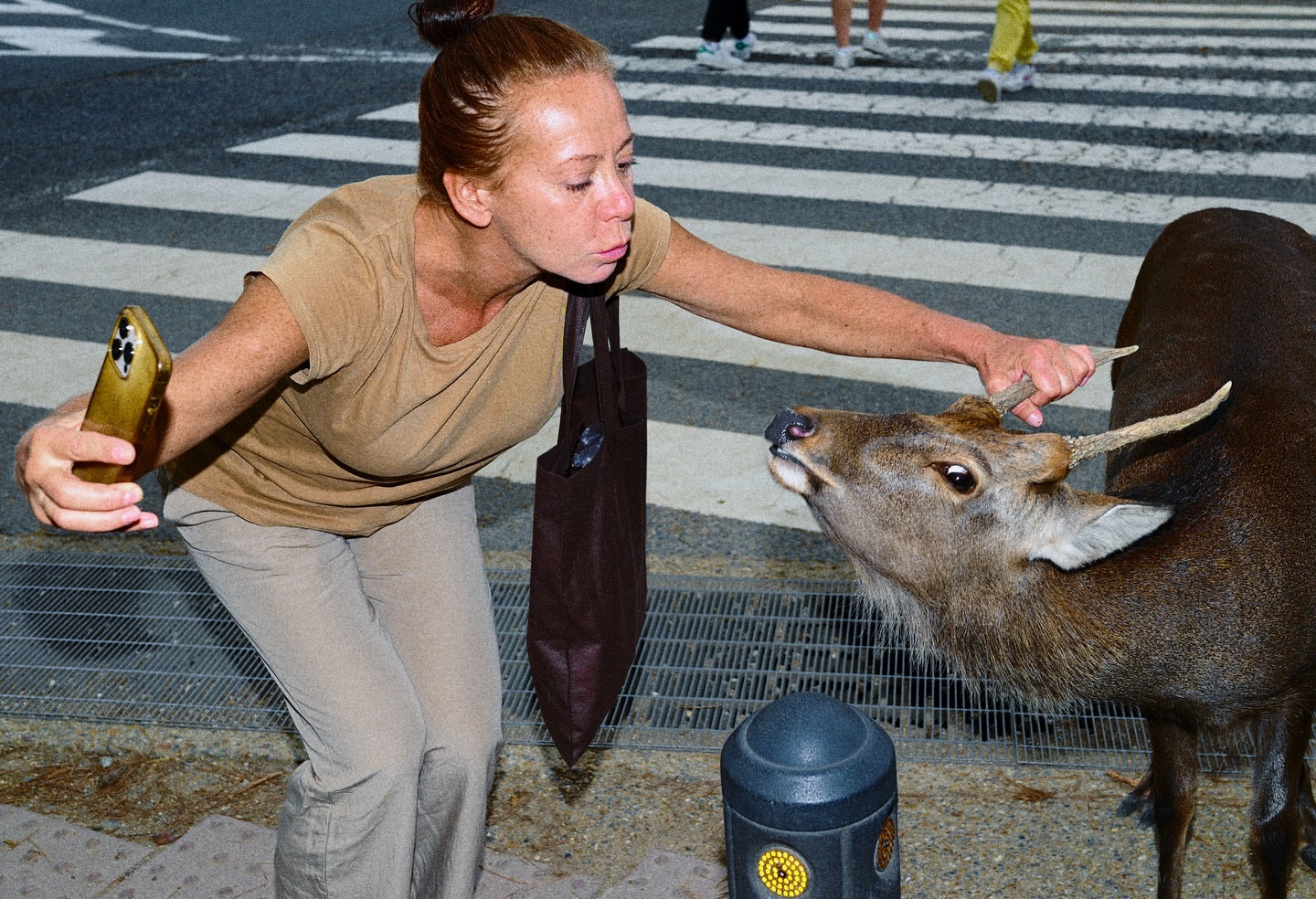 A woman taking a selfie while touching a deer's antler near a zebra crossing, photographed by Manu Jaime.