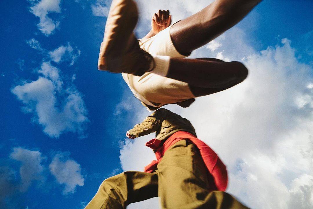 Low-angle shot of two people leaping against a vibrant blue sky with fluffy white clouds, capturing movement and dynamic energy.