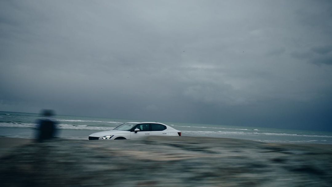 Car on a beach near the water with an overcast sky, moody coastal atmosphere and blurred foreground; automotive lifestyle content.