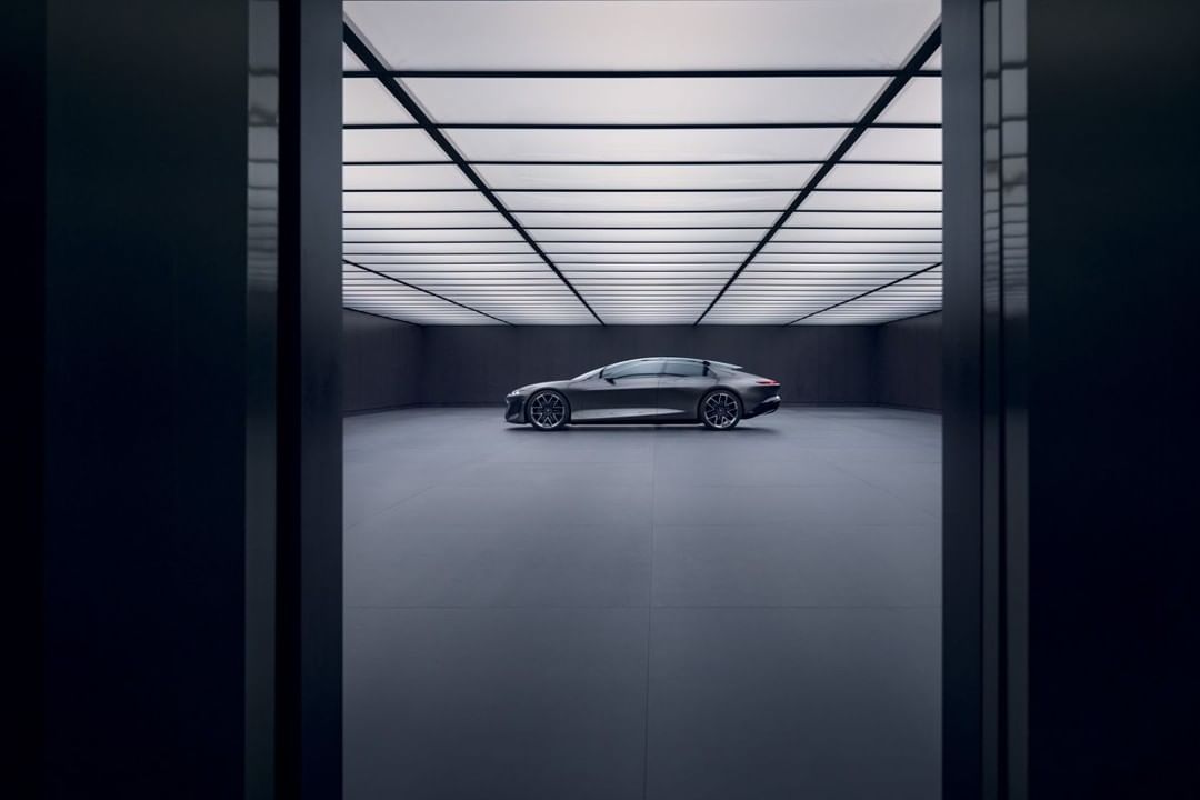 Sleek grey Audi e-tron GT parked inside a minimalist showroom with bright ceiling lights and a clean, modern aesthetic on a grey floor.