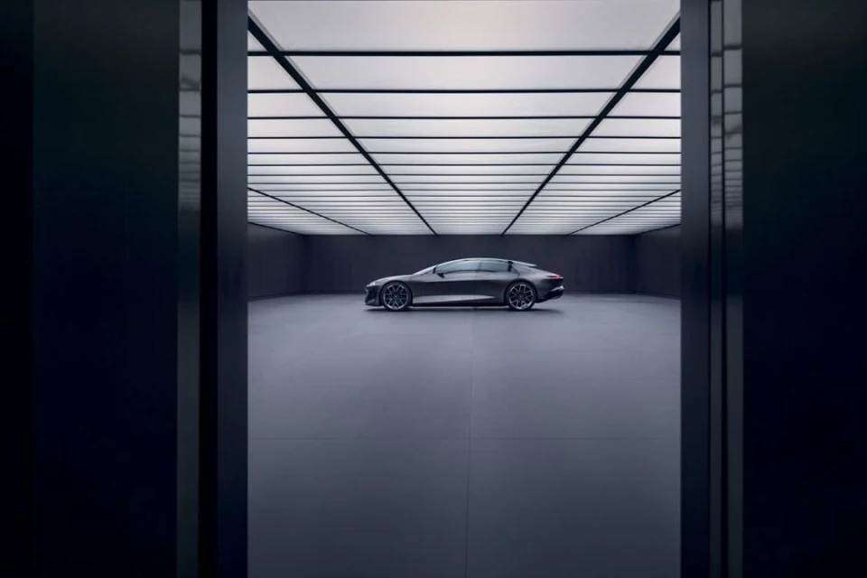 Sleek grey Audi e-tron GT parked inside a minimalist showroom with bright ceiling lights and a clean, modern aesthetic on a grey floor.