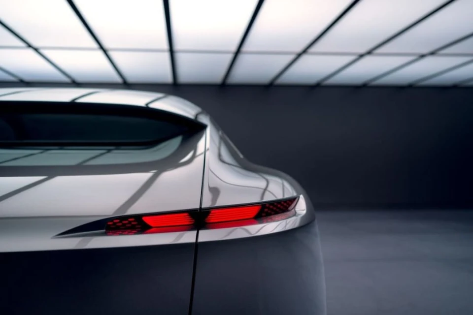 Rear view of a silver-grey car with striking red tail lights under bright studio lighting, highlighting automotive design and modern aesthetics.