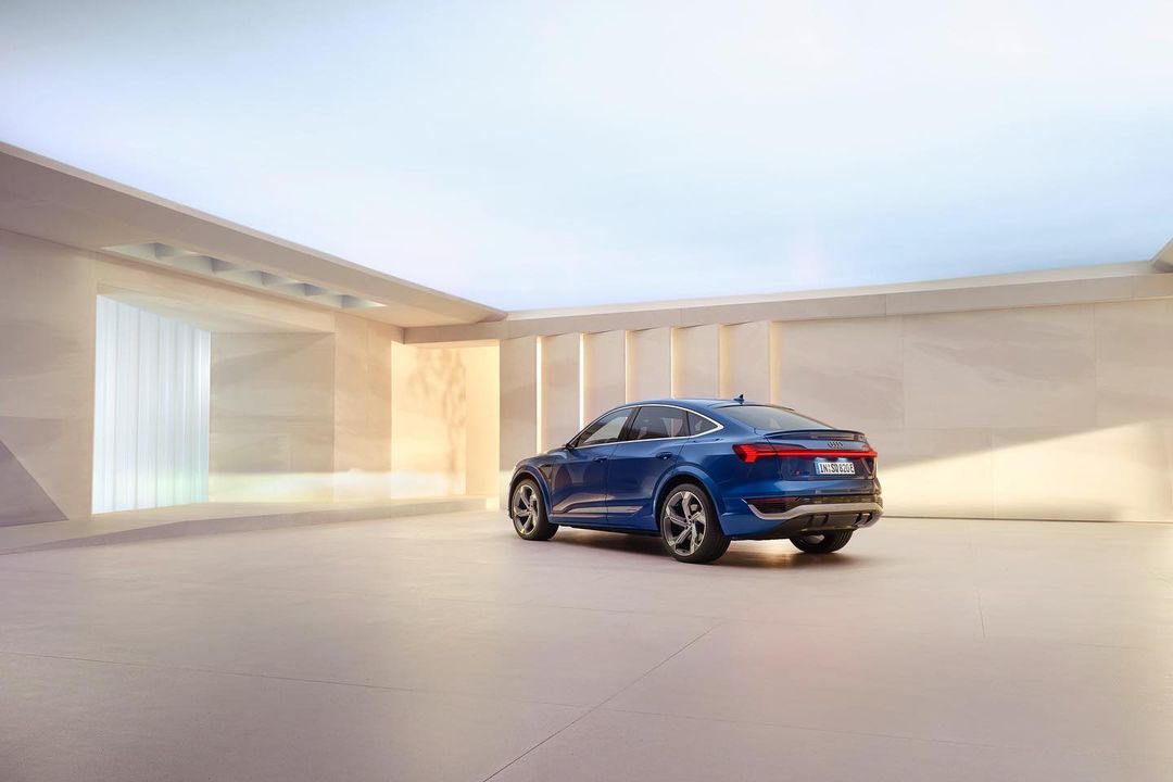 A blue Audi e-tron Sportback electric SUV is showcased in a minimalist studio with bright, even lighting and a spacious, reflective floor.