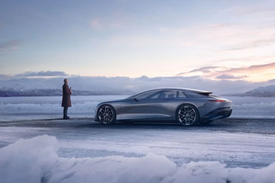 Sleek grey car stands out against a snowy landscape near mountains as a man looks at it in a scenic outdoor automobile shoot.