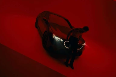 Man standing next to a dark luxury sedan in a dramatic red studio environment by Manuel Nagel