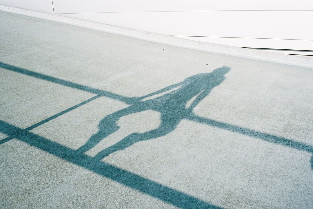 Shadow of a person walking on a concrete walkway next to a wall, cast by bright sunlight, creating long shadows on the ground.