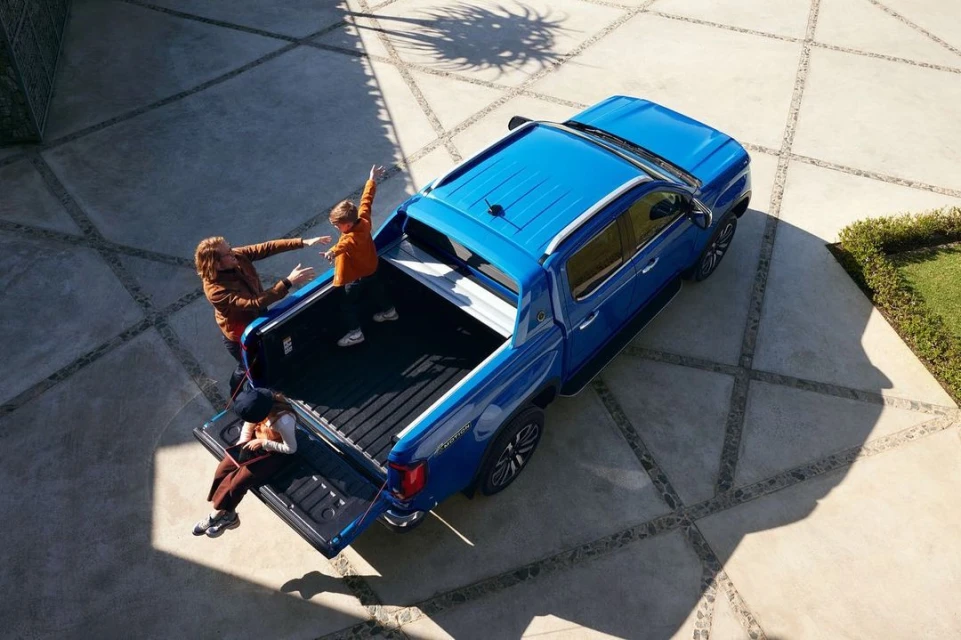Aerial view of a blue pickup truck parked on a patterned driveway with an adult male, female, and child in the truck bed.