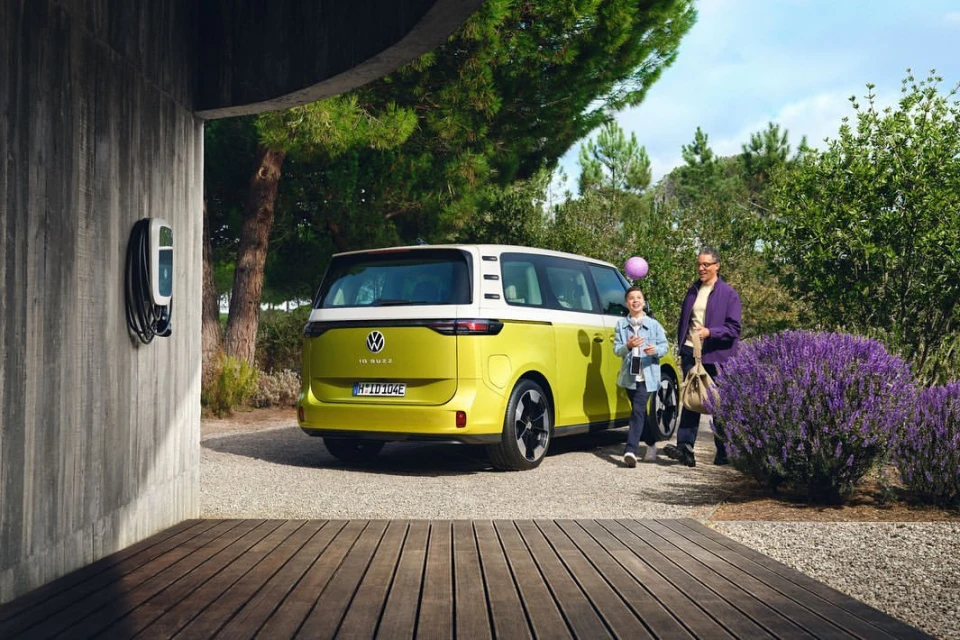 Yellow and white Volkswagen ID Buzz electric van parked outside a modern home with a father and child standing nearby on a sunny day.