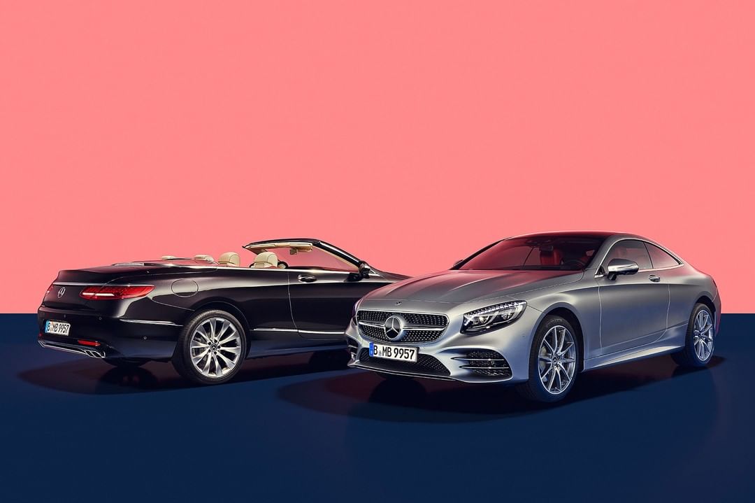 Silver hardtop and black convertible Mercedes-Benz cars with a coral and navy backdrop, showcasing automotive design and luxury.