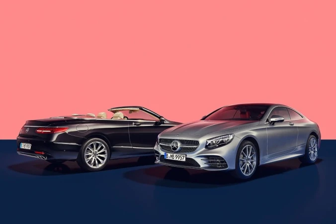 Silver hardtop and black convertible Mercedes-Benz cars with a coral and navy backdrop, showcasing automotive design and luxury.