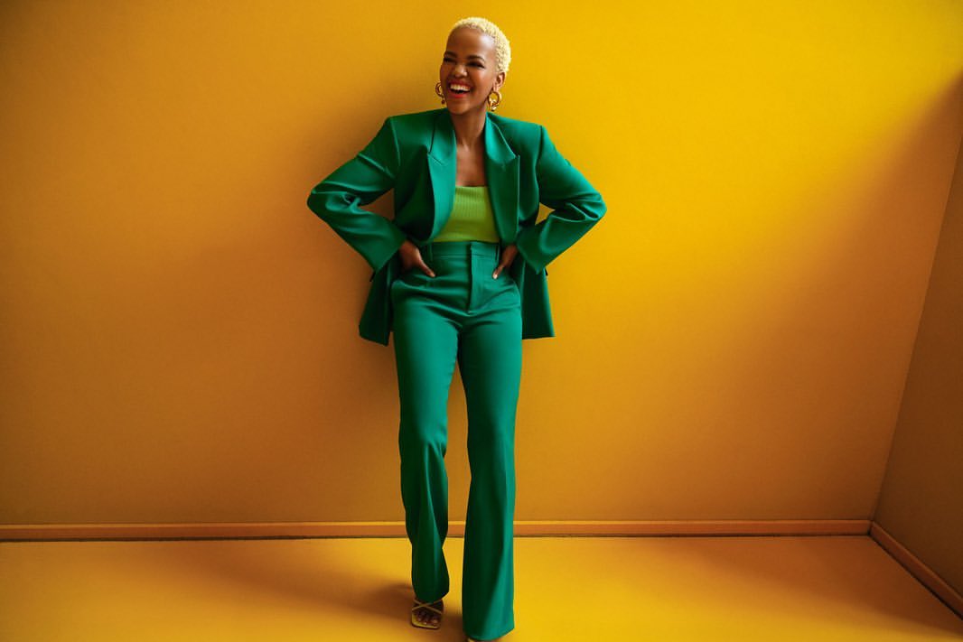Stylish woman in green suit smiles against a bright yellow background. Portrait of a fashion model with short hair in studio.