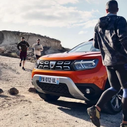 Bright orange SUV parked on a dusty dirt trail with runners outdoors under a sunny sky
