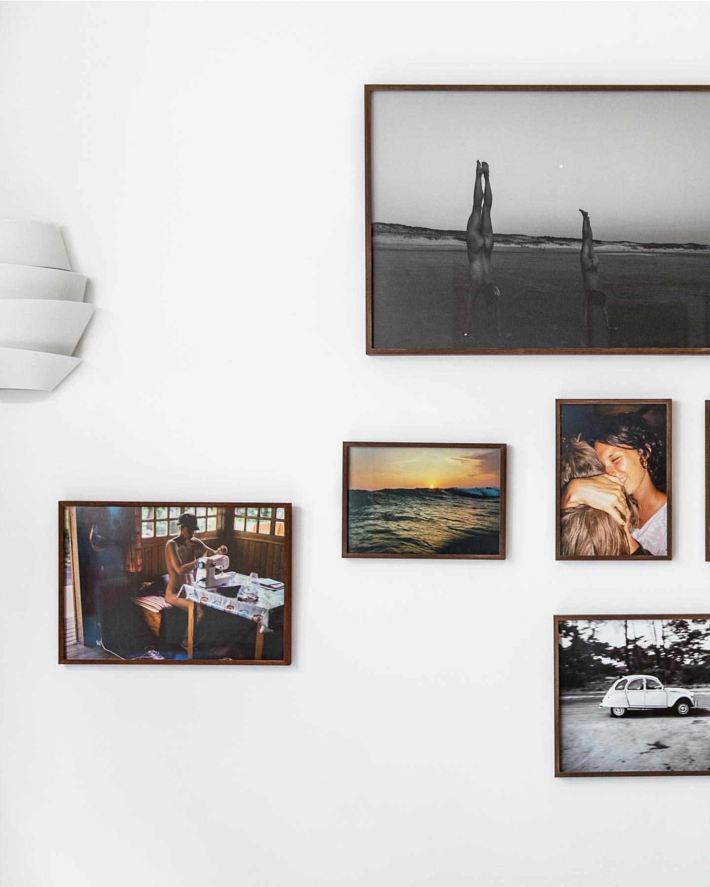 Interior wall with an arrangement of framed photographic prints, featuring beach scenes, portraits, and interior scenes with natural light.