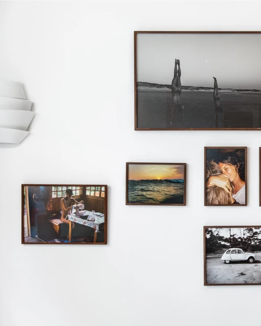 Interior wall with an arrangement of framed photographic prints, featuring beach scenes, portraits, and interior scenes with natural light.