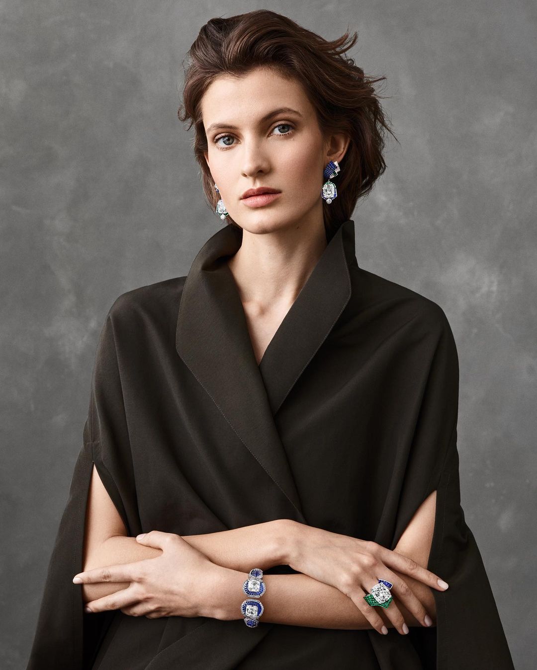 Portrait of a brunette woman wearing a formal black dress and fine jewelry, including earrings, a bracelet, and a ring.