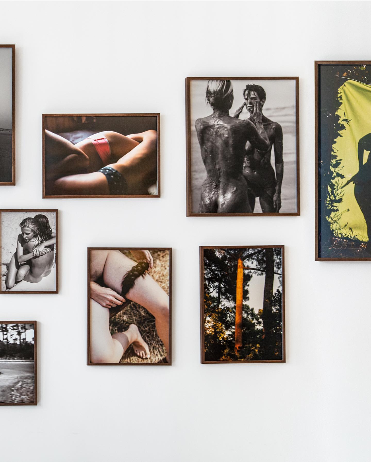 Photographs of people, landscapes, and nature hang in a grid-like arrangement on a plain white wall in a minimalist interior setting.
