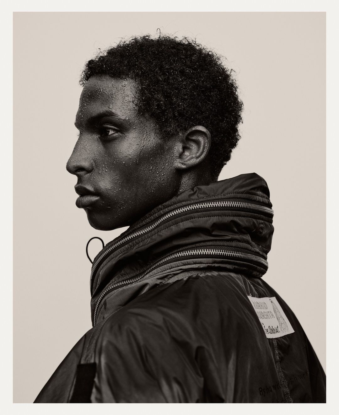 Profile portrait of a young Black man with water droplets on his skin, wearing a dark puffer jacket.