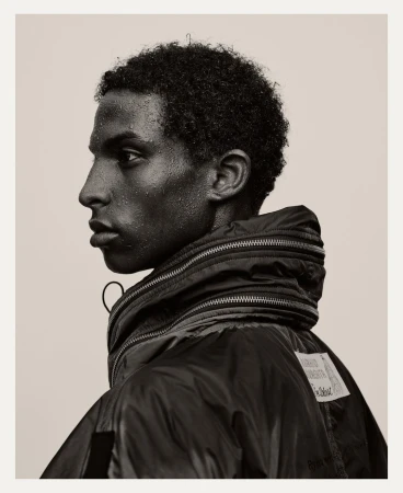 Profile portrait of a young Black man with water droplets on his skin, wearing a dark puffer jacket.