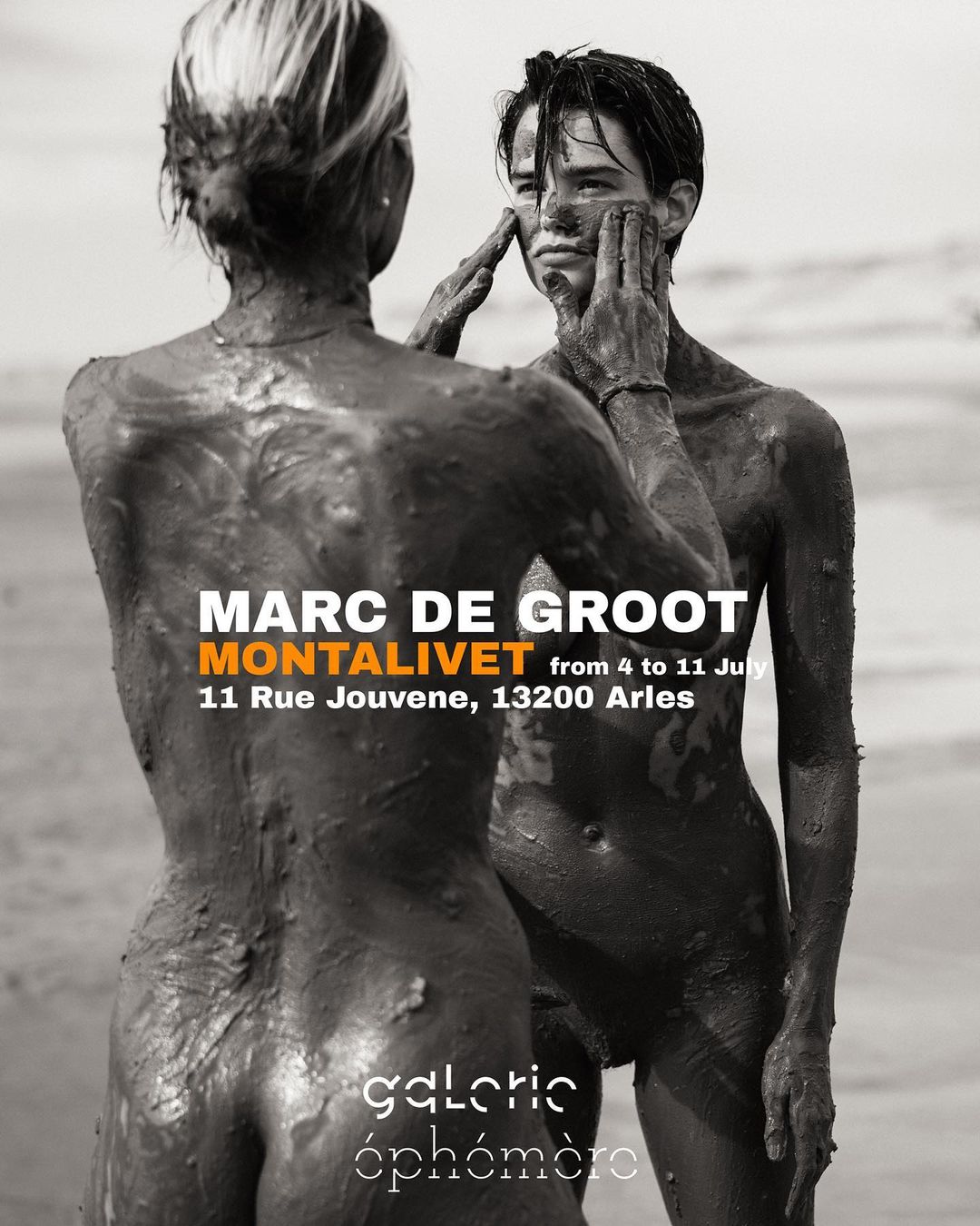 Two nude figures covered in mud pose on a beach in this high-contrast black and white promotional image for an art exhibition.