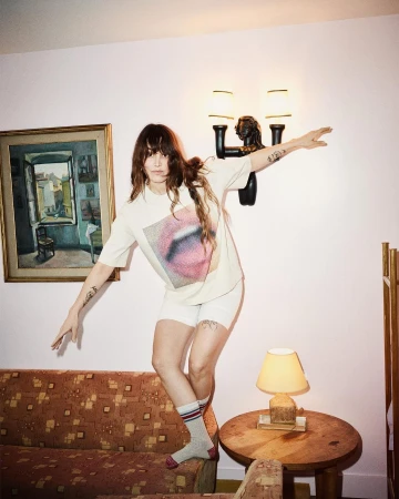 Woman in graphic t shirt and shorts posing on a patterned sofa by photographer Marc De Groot in Paris.
