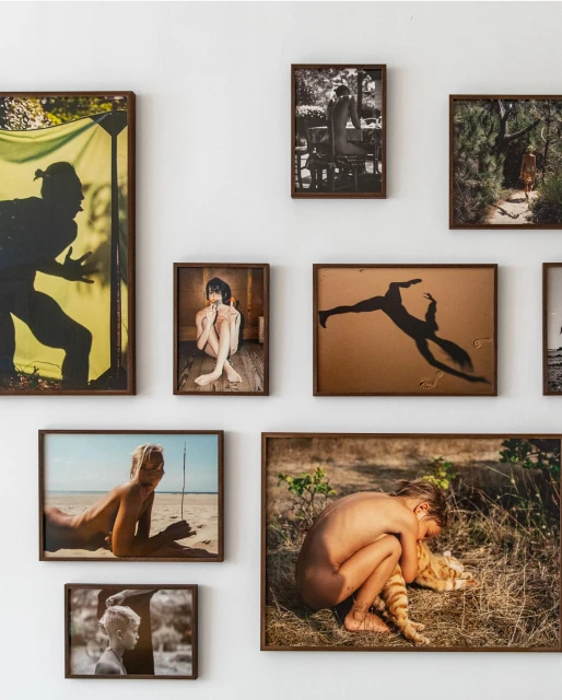 Collection of framed photographs on a white wall, showcasing various subjects including a silhouette, nude figures, and outdoor scenes.