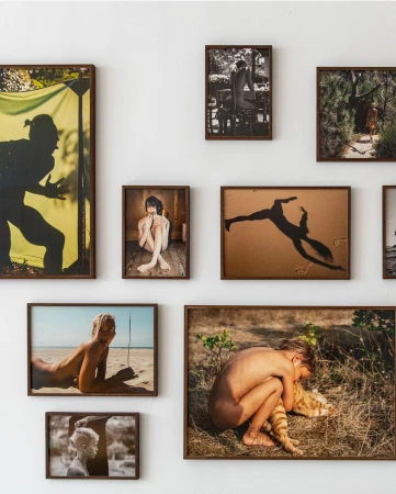 Collection of framed photographs on a white wall, showcasing various subjects including a silhouette, nude figures, and outdoor scenes.