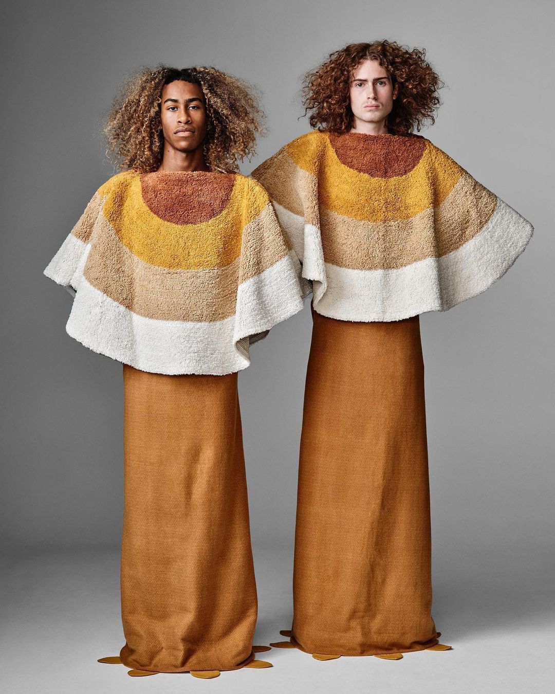 Two adult models showcasing striped textile tops and brown skirts, posed in a studio setting against a plain gray background.