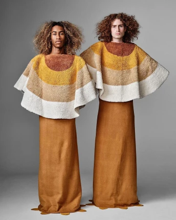Two adult models showcasing striped textile tops and brown skirts, posed in a studio setting against a plain gray background.