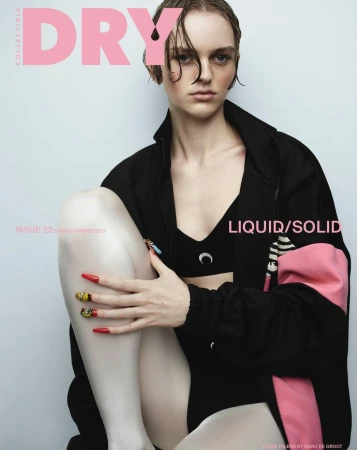 Model with wet hair wearing a black athletic jacket and cropped top against a light grey studio background.