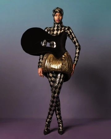 Full-length shot of a fashion model in a futuristic, harlequin-patterned costume against a blue and purple gradient background.