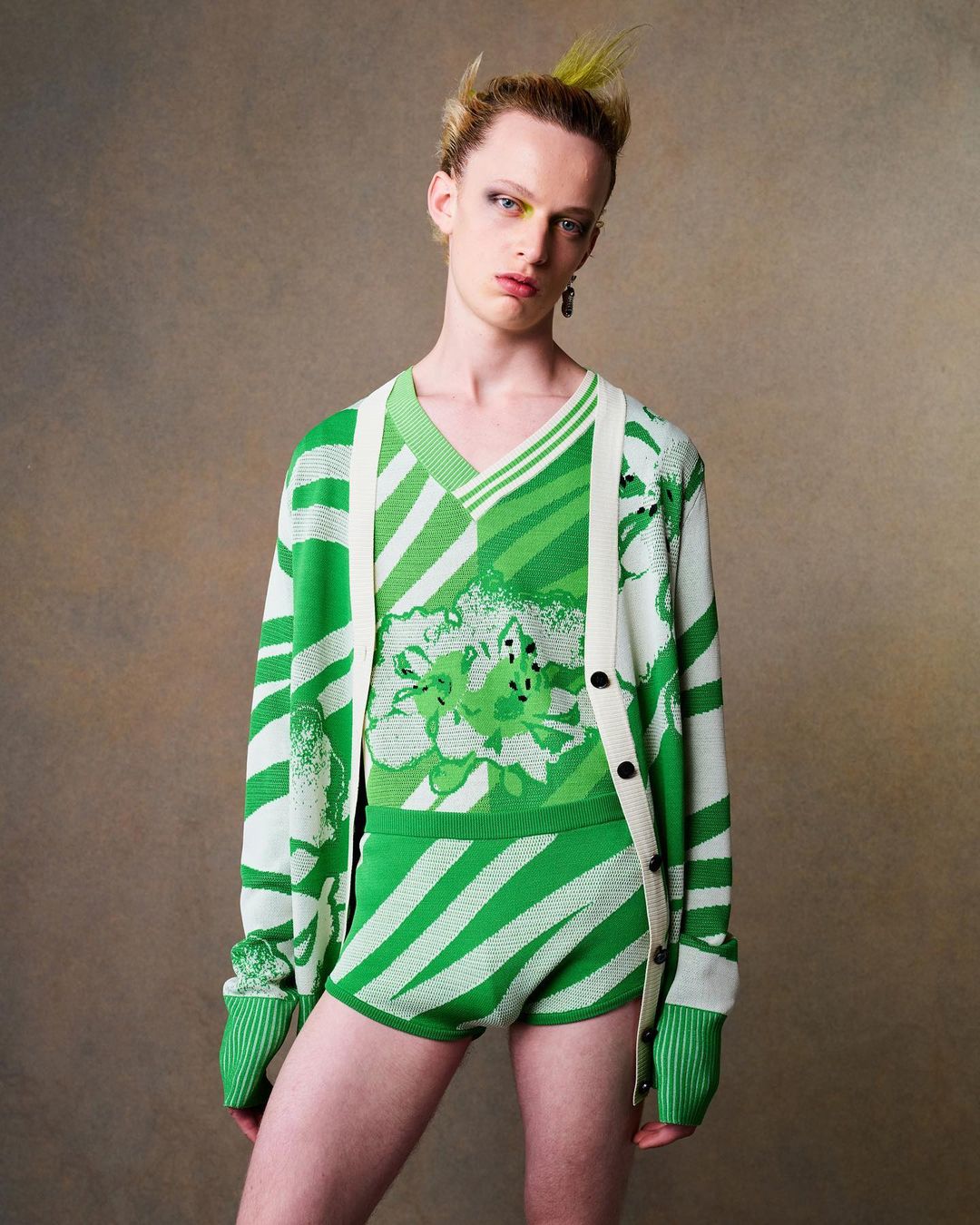 Androgynous person in green and white patterned knitwear poses in a studio with a neutral background. Fashion and style.