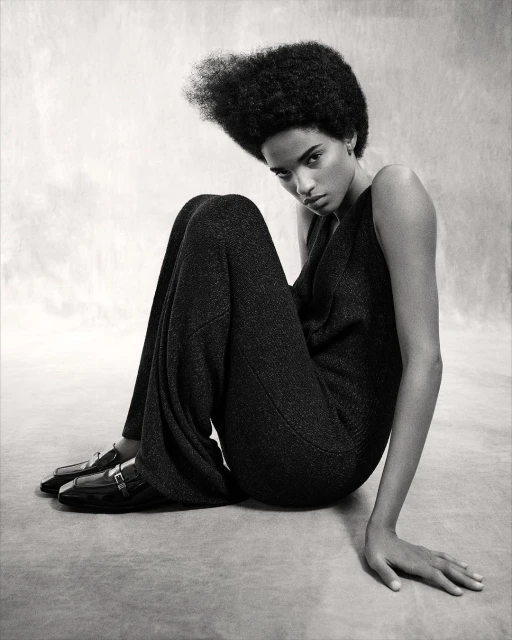 Elegant Black and White Studio Portrait of a Solo Adult Female Model with an Afro Wearing Dark Jumpsuit and Patent Leather Loafers.