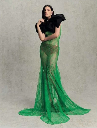 Model in green sheer lace gown with dramatic black ruffled collar posing against a textured grey background by Marc Hibbert